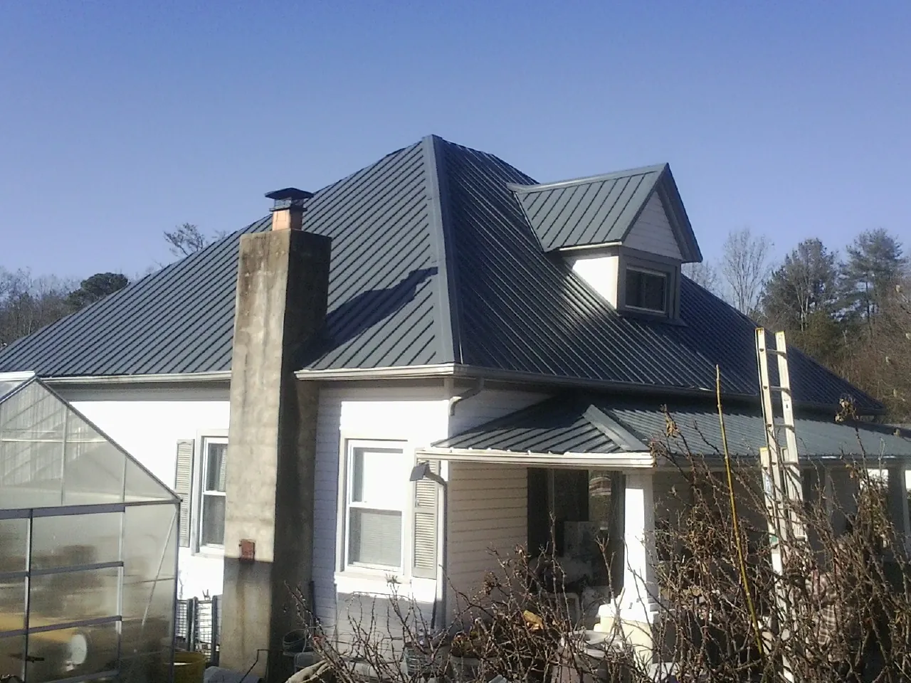 Dark blue standing seam metal roof on a white farmhouse with dormer — Slate & Tile Roof Repair by Roofing Brothers in Gassaway