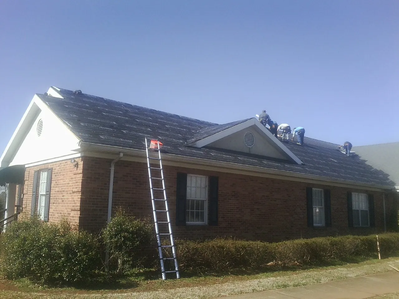 Crew tearing shingles off a brick ranch roof with a ladder set — Emergency Roof Repair work by our crew in Gassaway
