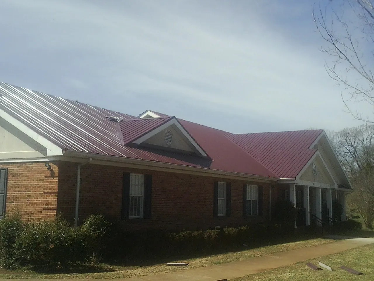 Red metal roof with gabled entries on a long brick building, from a Hail Damage Roof Repair job in Gassaway