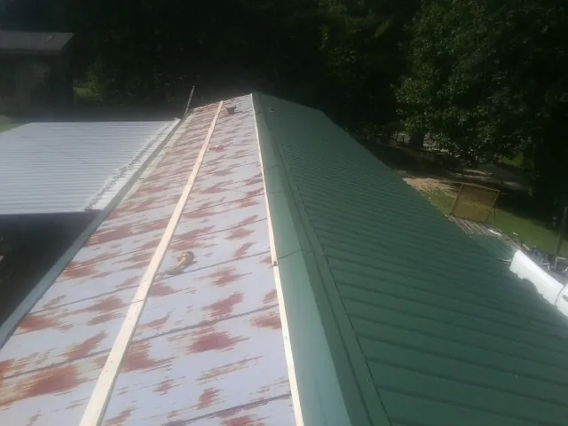 Old rusted panels beside newly installed green metal roofing — Wind Damage Roof Repair by Roofing Brothers in Gassaway