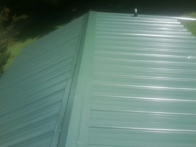 New green metal panels meeting at the ridge of a roof — Flat Roof Repair work by our crew in Gassaway