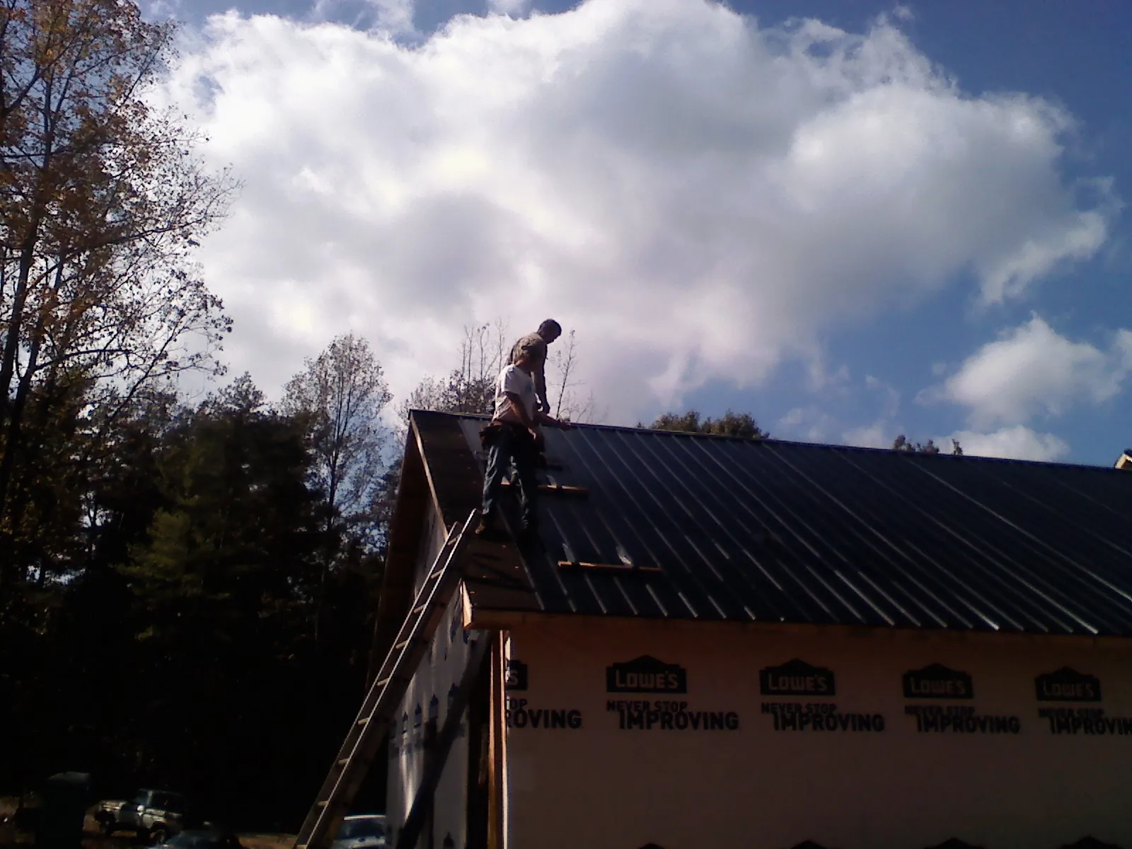 Roofer fastening dark metal panels high against a cloudy sky, from a Roof Inspection job in Gassaway