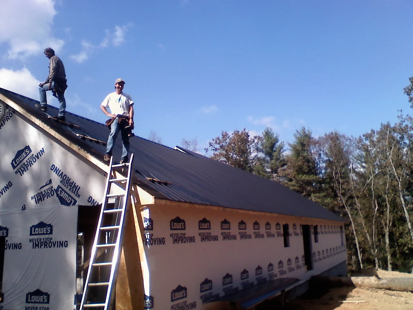 Two roofers standing on a long dark metal roof over a wrapped building in Gassaway
