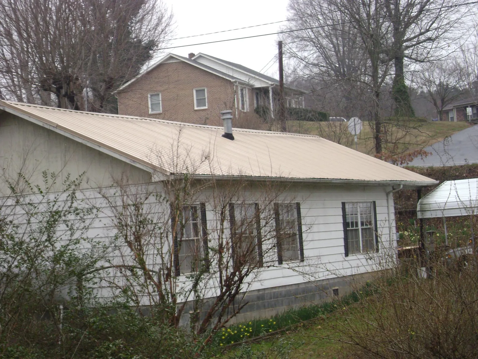 Tan metal roof on a white sided house set into a hillside — Commercial Roofing by Roofing Brothers in Gassaway