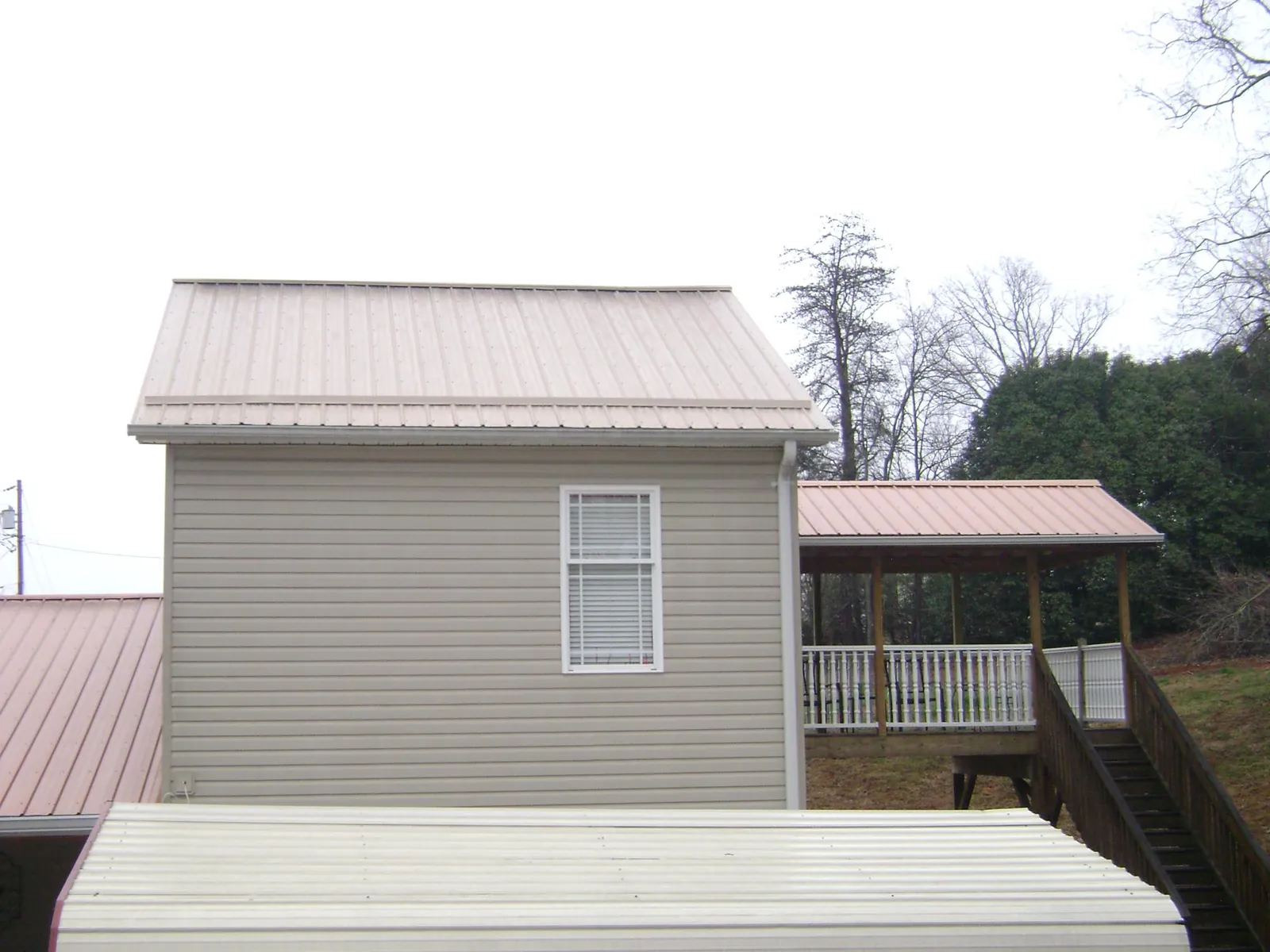 Tan metal roofs on a two story addition and attached porch, from a Roof Replacement job in Gassaway